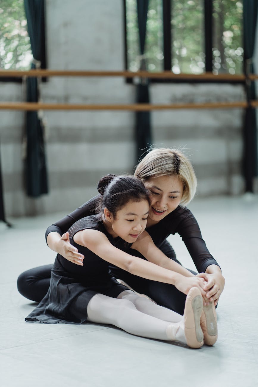 asian female ballet instructor helping ballerina girl to stretch body